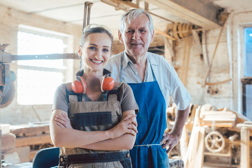 Maître charpentier senior avec sa petite-fille dans l'atelier de menuiserie regardant la caméra.