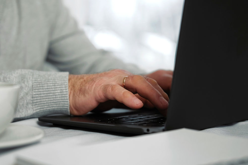 Gros plan des mains d'un homme âgé utilisant un ordinateur portable. Vue latérale recadrée de mains caucasiennes âgées et ridées tapant sur le clavier. Personnes âgées avec la technologie. Homme retraité méconnaissable travaillant à domicile, assis à un bureau.